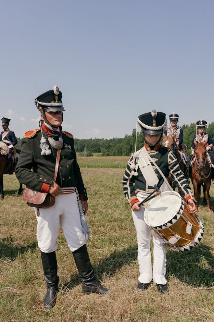 soldiers-an-a-drummer-in-historical-uniforms-9270568 A group of historical reenactors in military uniforms stands in a field, with one playing a drum.